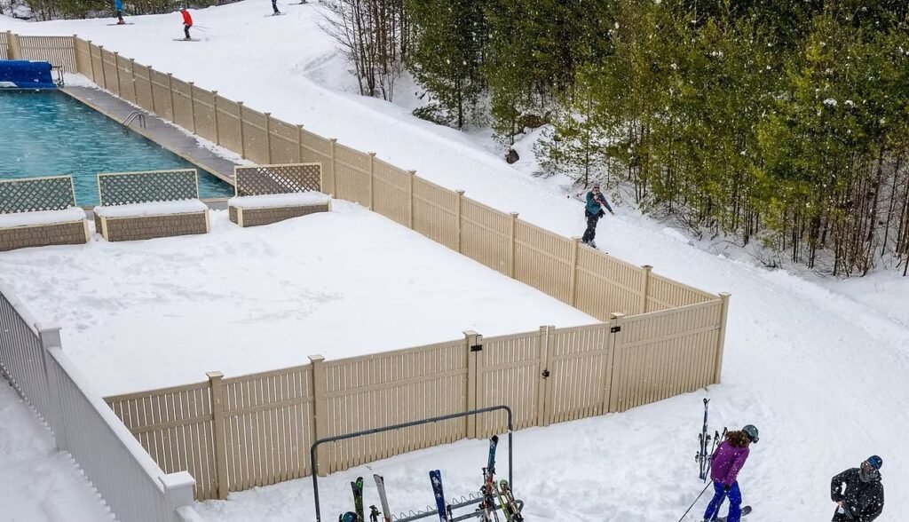 Snow-covered outdoor pool and hot tub area at Grand Summit Hotel in Bartlett, New Hampshire with nearby ski access, fencing, and scenic wooded surroundings in the White Mountains during winter.